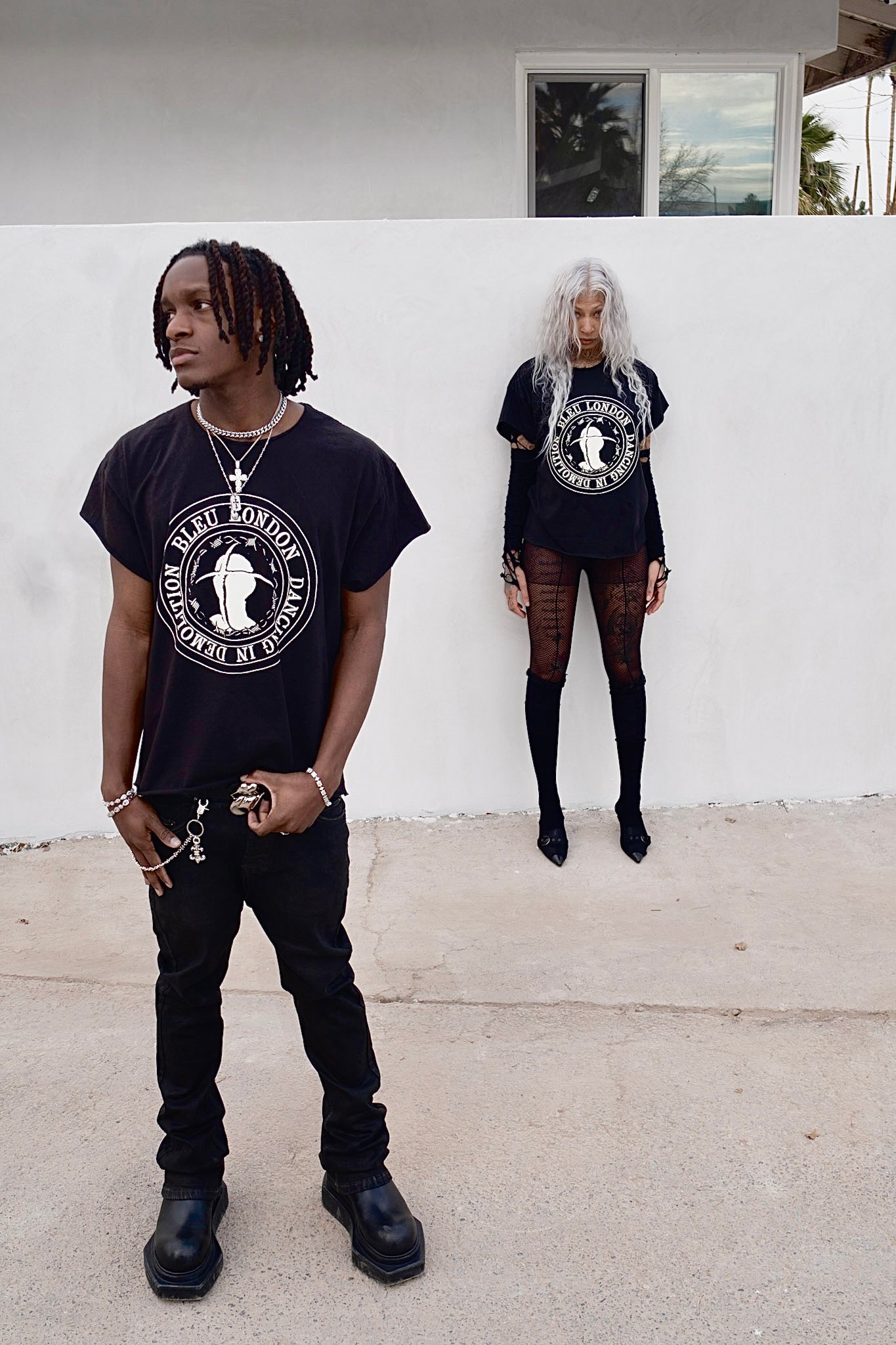 Two people wearing black t-shirts with graphic designs standing in front of a white wall.