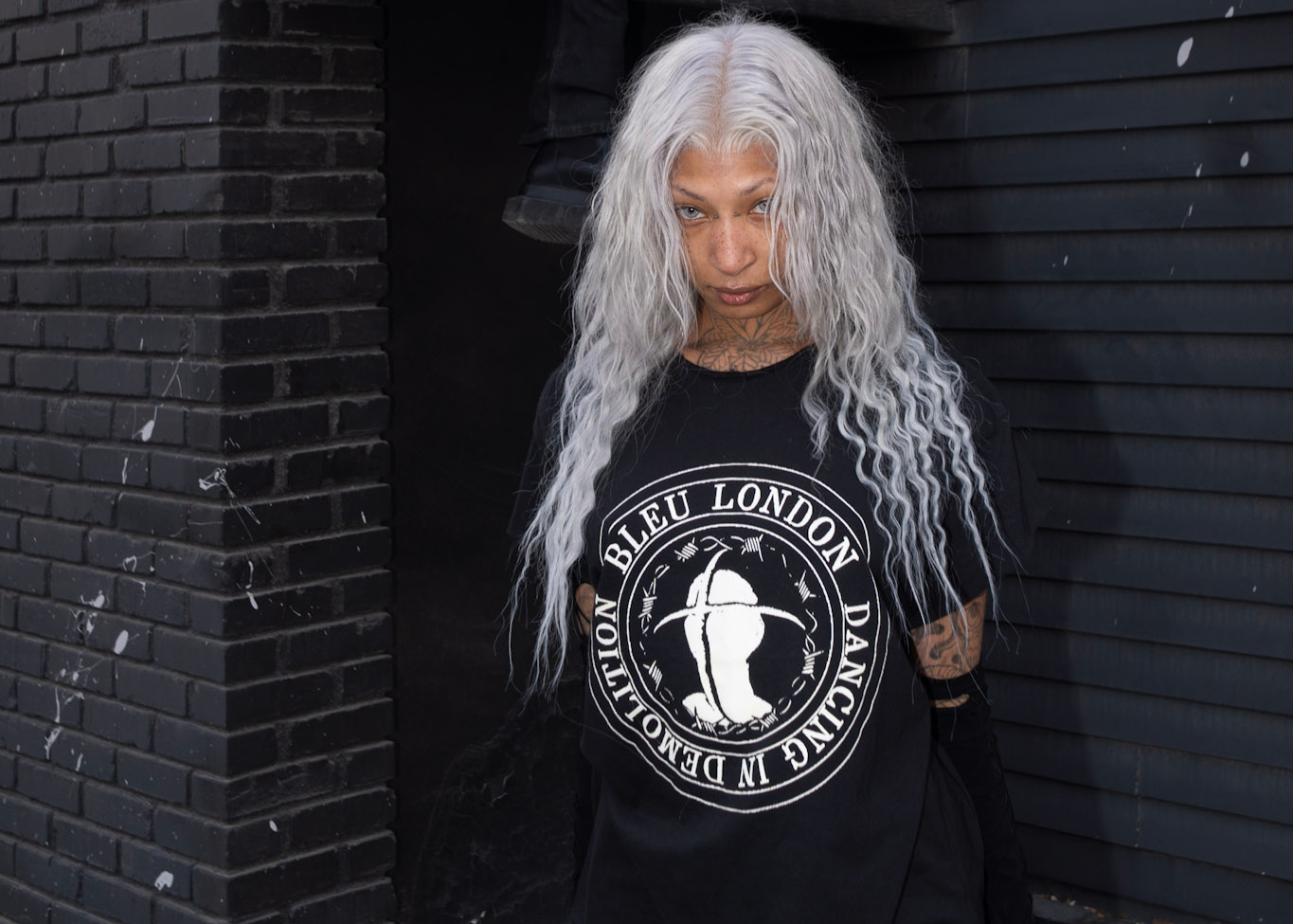Two people wearing black t-shirts with logos against a dark building.